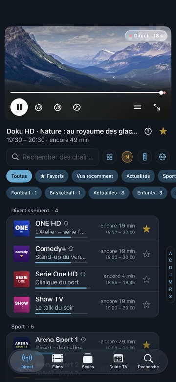 L’écran d’accueil de Neverlag sur iPhone : en haut la chaîne en cours avec la barre du lecteur et le compteur, puis la recherche, des filtres comme Favoris, Football et Actualités, et la liste des chaînes par groupe avec le temps restant